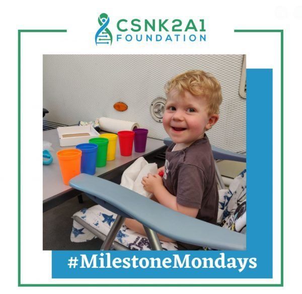 A young girl is holding a plate of food with the words milestone mondays below her