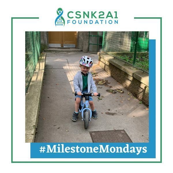 A young boy wearing a helmet is riding a bike on a sidewalk sponsored by the csnk2a1 foundation