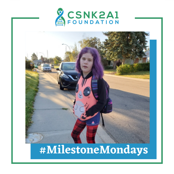 A girl with purple hair is standing on a sidewalk in front of a csnk2a1 foundation logo