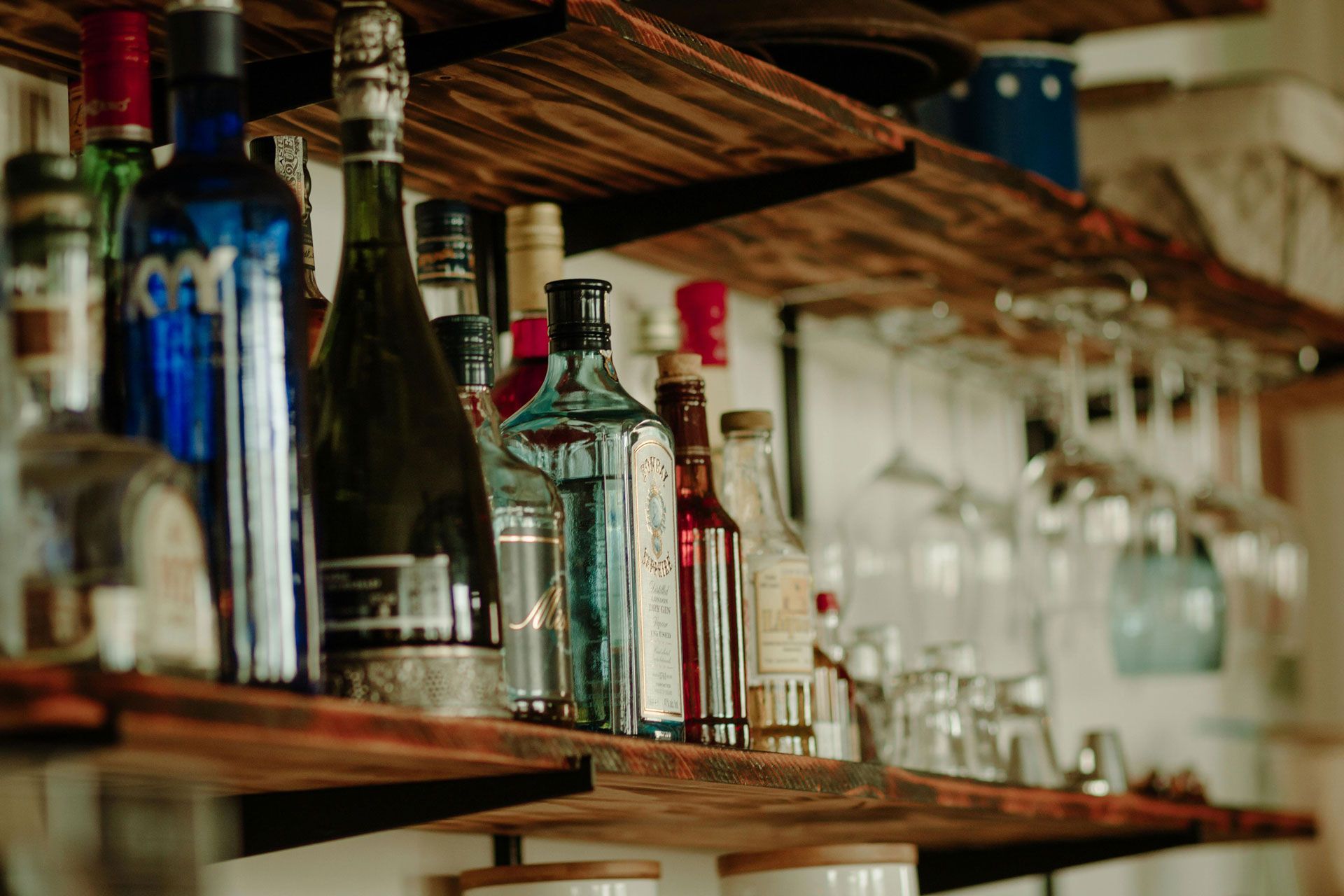 A collection of various liquor bottles and glassware displayed on wooden shelves at a bar.
