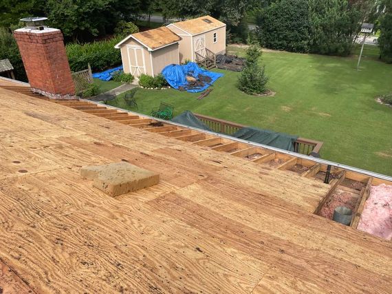 An aerial view of a roof with a chimney and a house in the background.