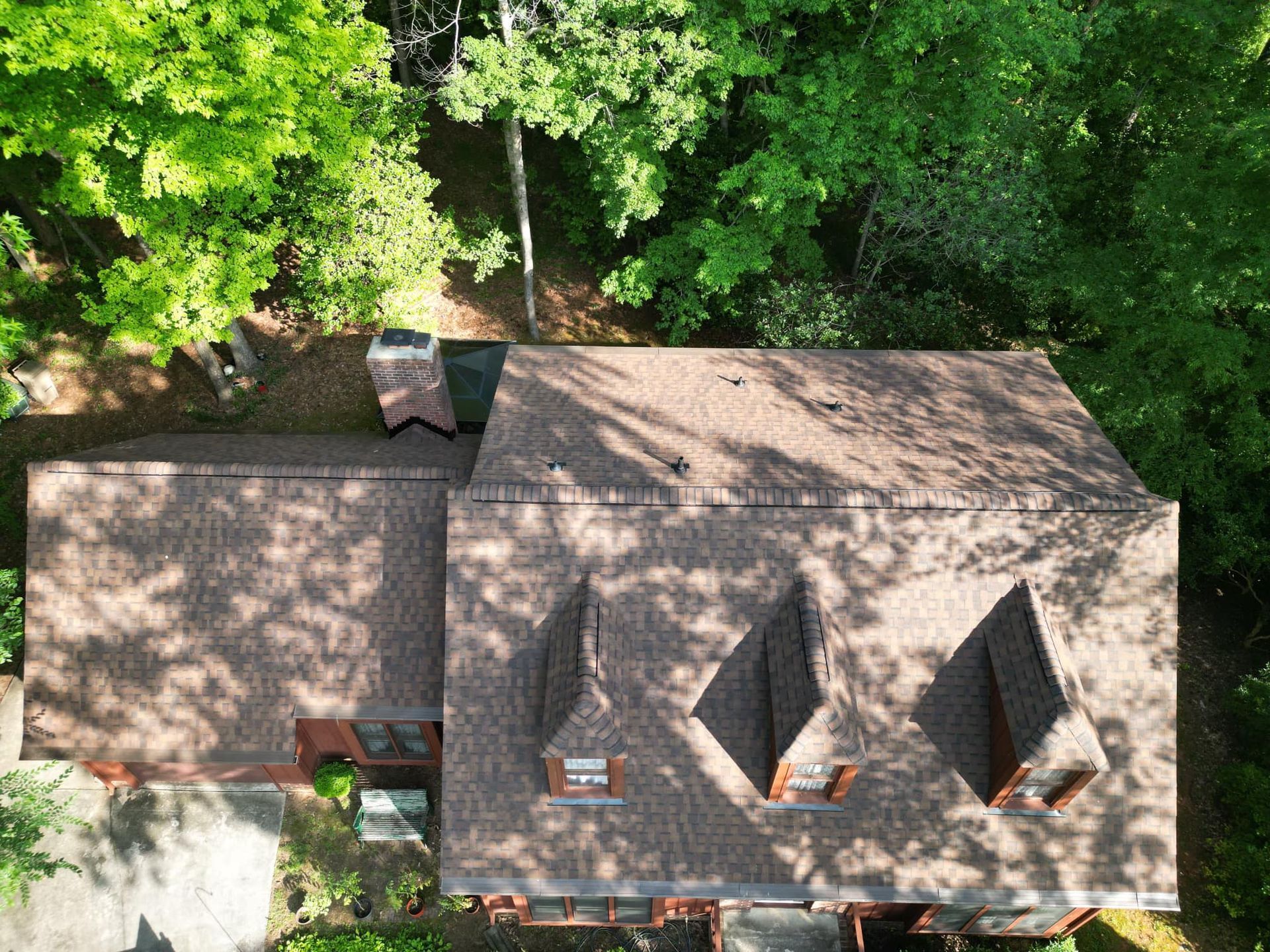 An aerial view of a house with a roof that is surrounded by trees.
