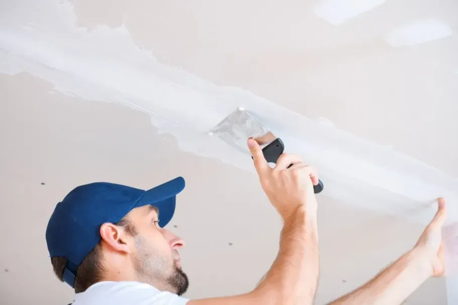 Painter applying white paint to a ceiling with a roller brush