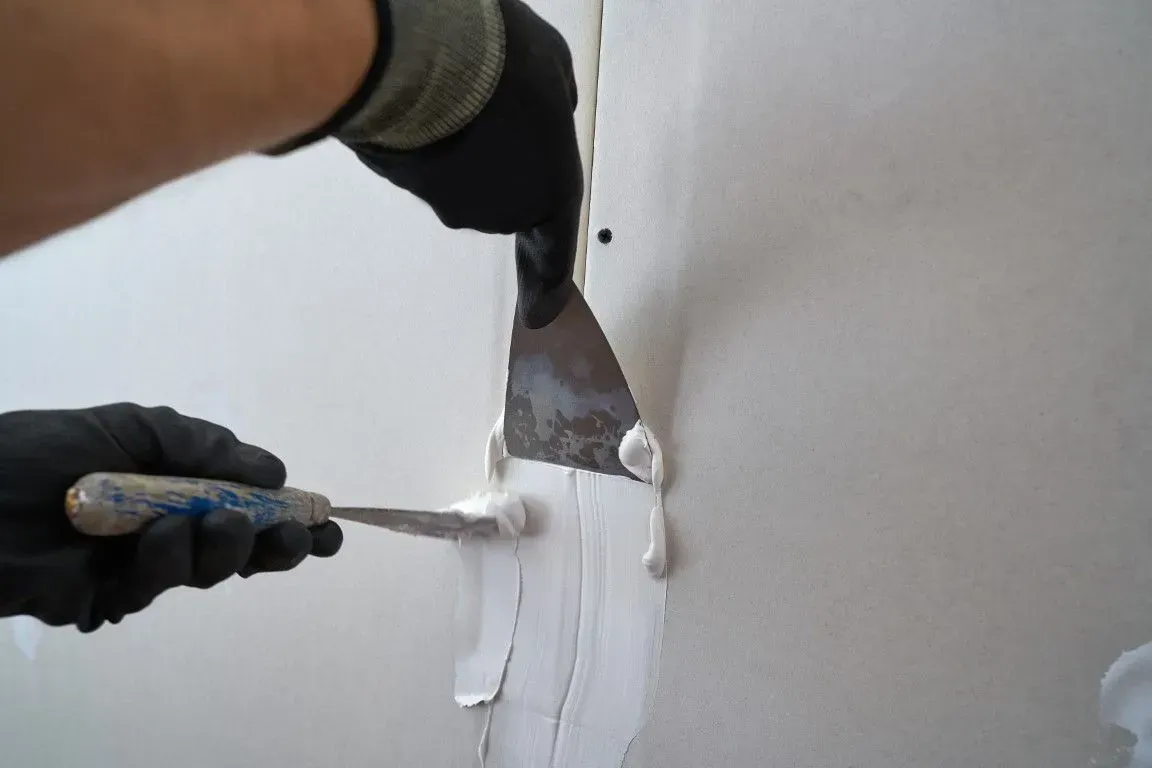 Hand using a putty knife to apply compound to a drywall crack.