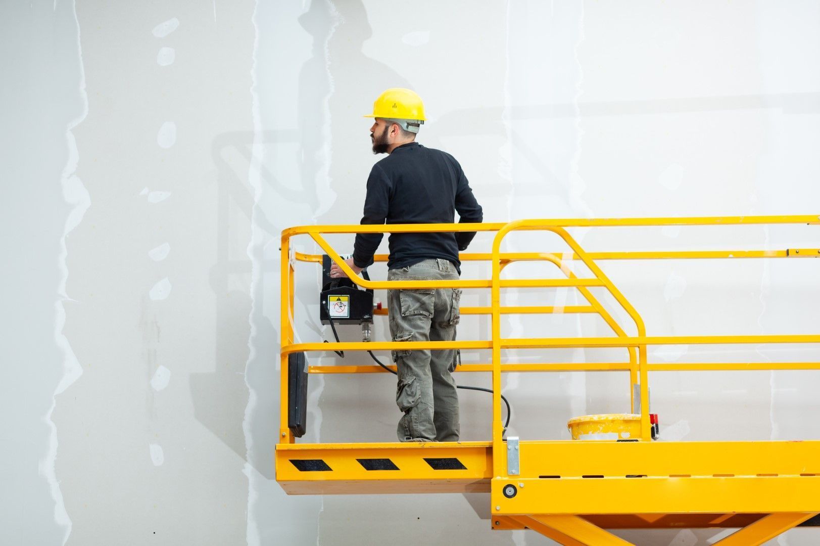 Worker on a yellow lift installing high drywall panels.