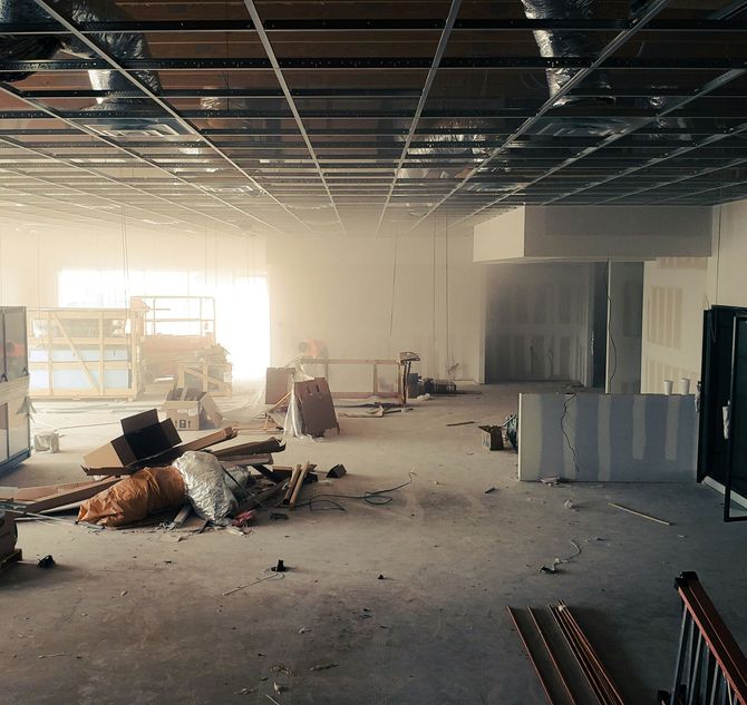 Abandoned office interior with debris on the floor, exposed ceiling grid, and bright light from windows.