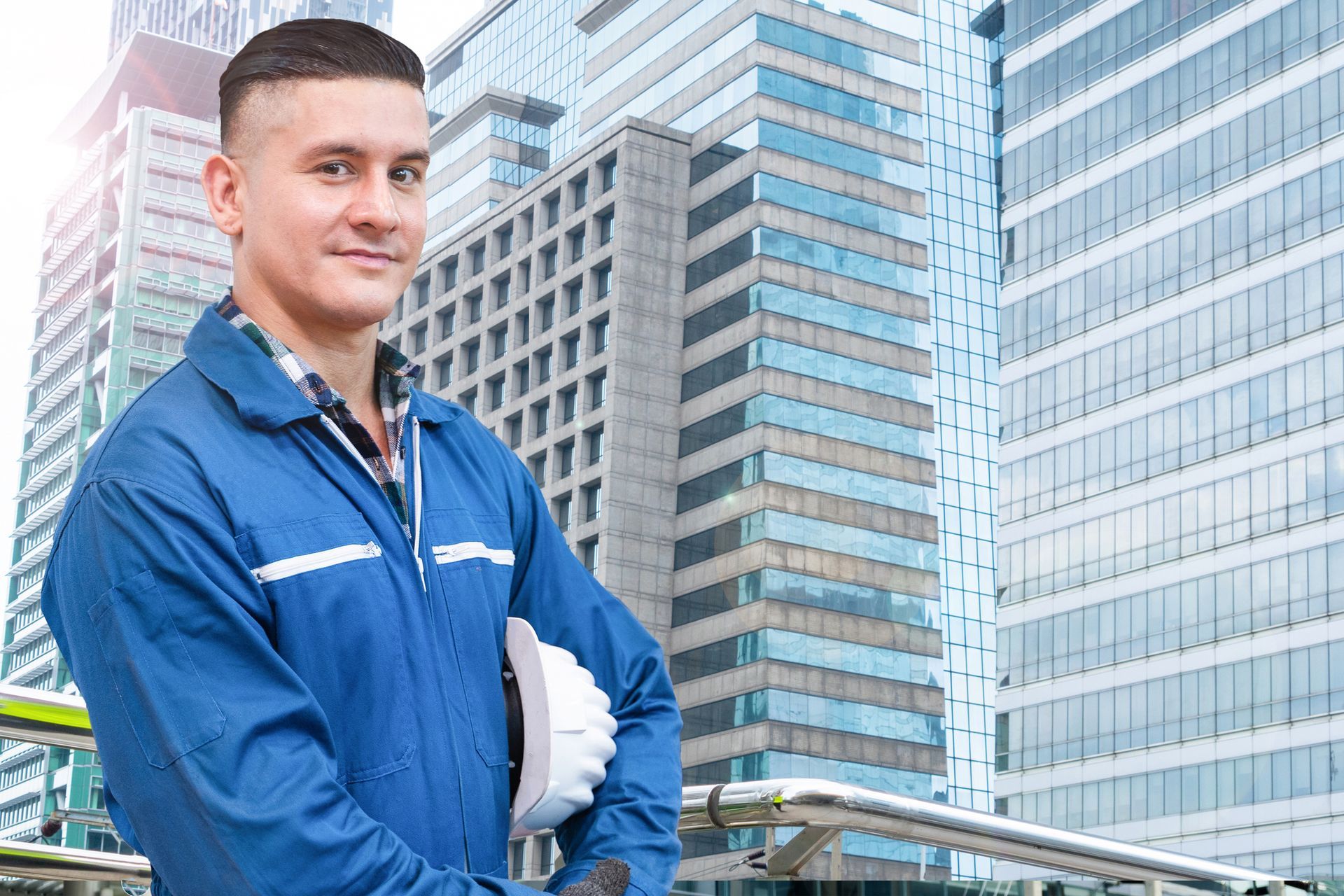 A man in a blue jacket is standing in front of a building holding a hard hat.