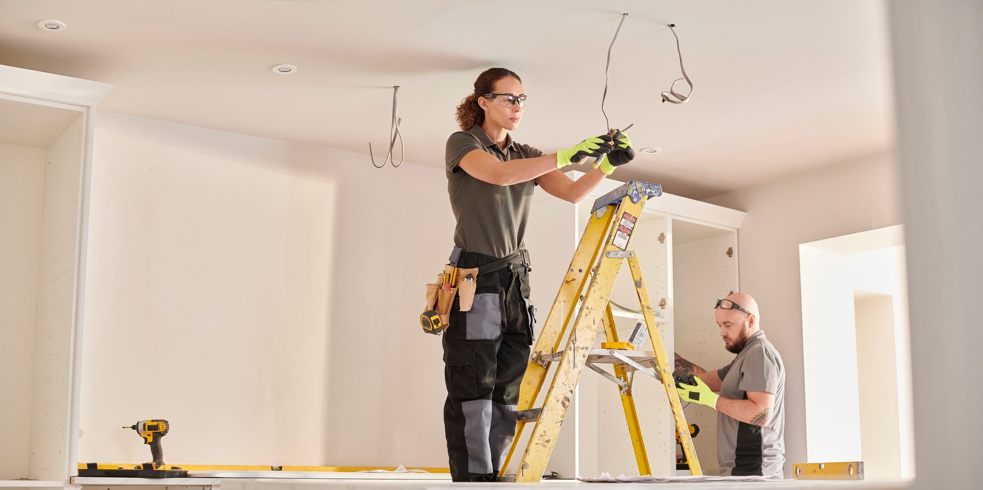 A man and a woman are working on a ceiling in a room.