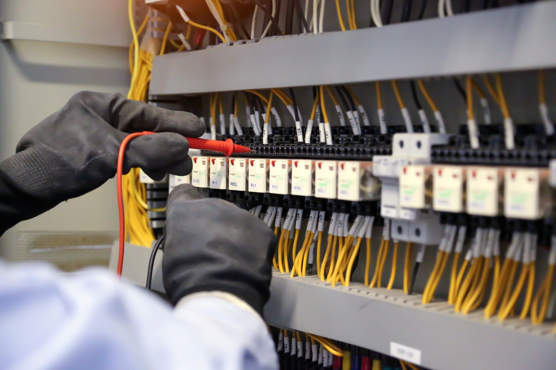 A man is working on an electrical panel with a voltmeter.