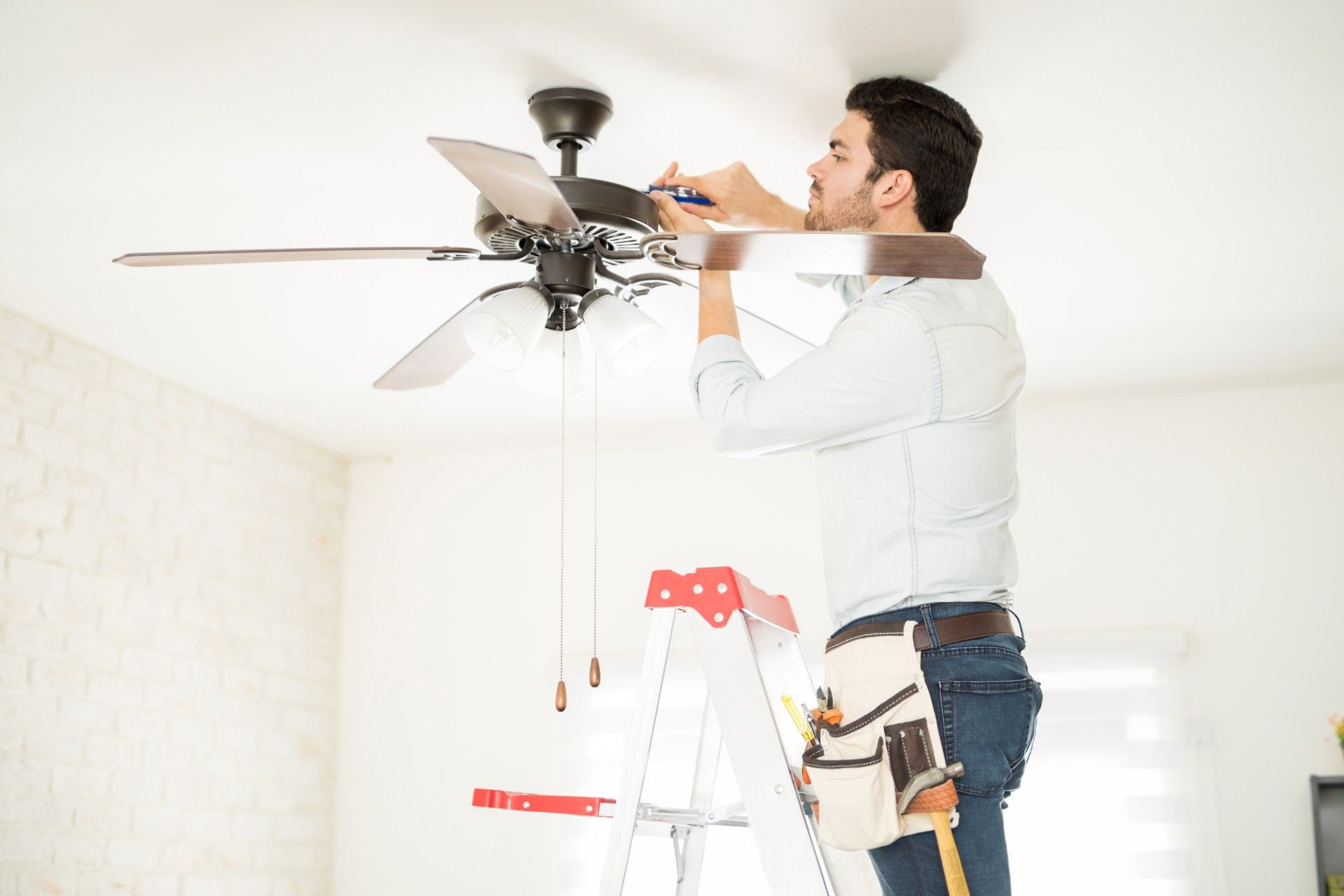 A man is standing on a ladder fixing a ceiling fan.