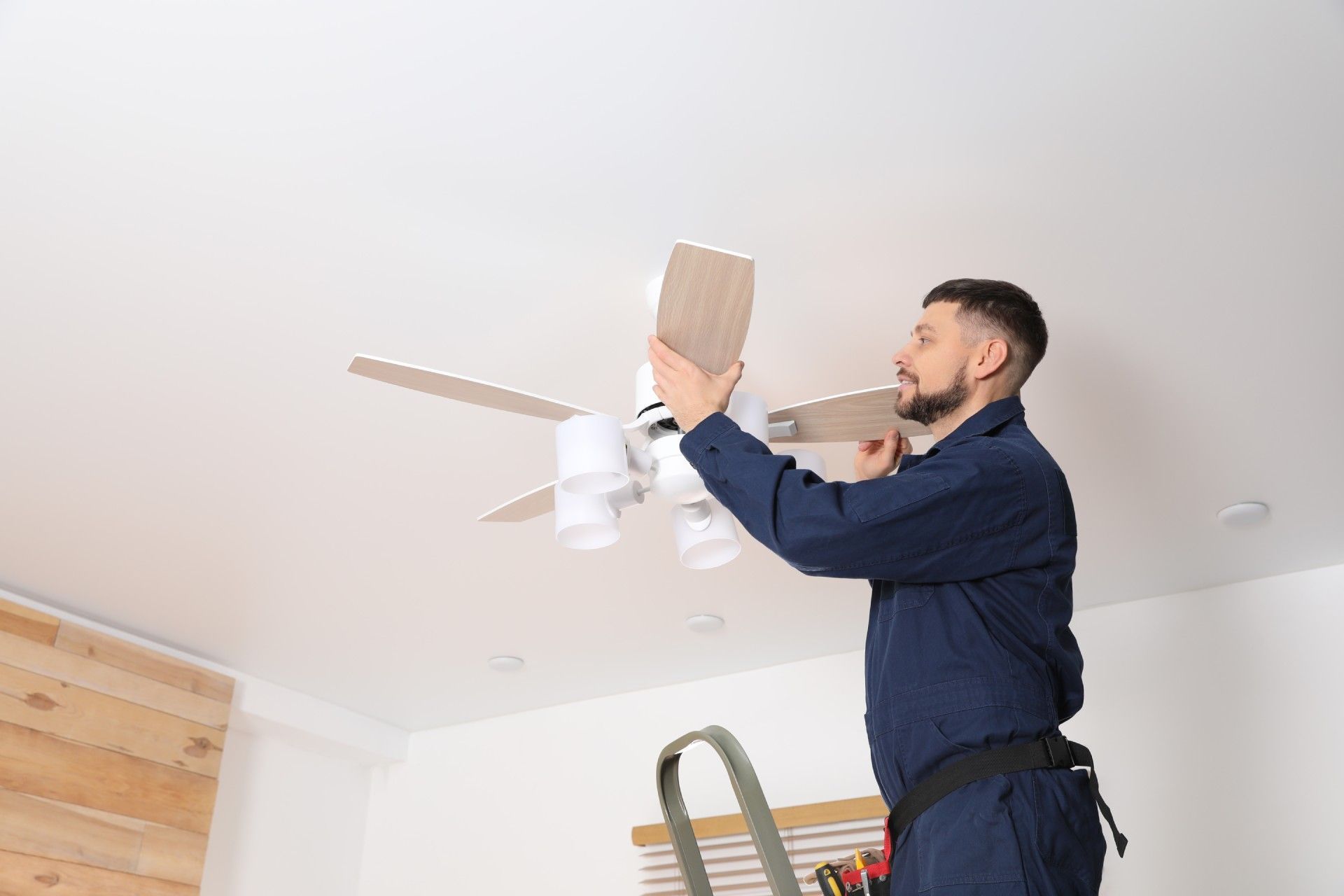 A man is installing a ceiling fan in a living room.