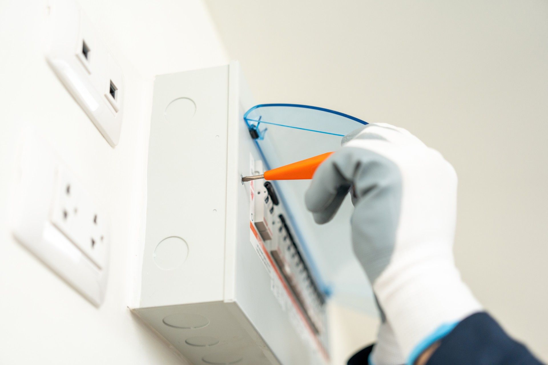 A person wearing white gloves is working on an electrical box