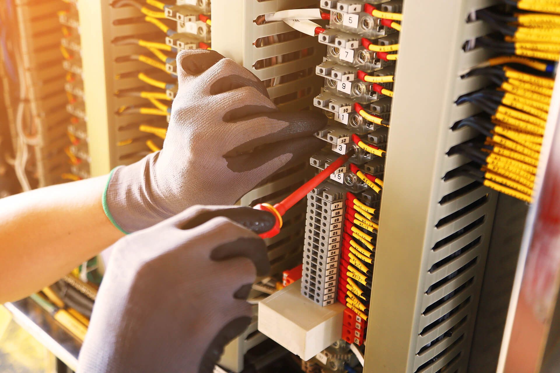 An electrician is working on an electrical panel with a pair of pliers.