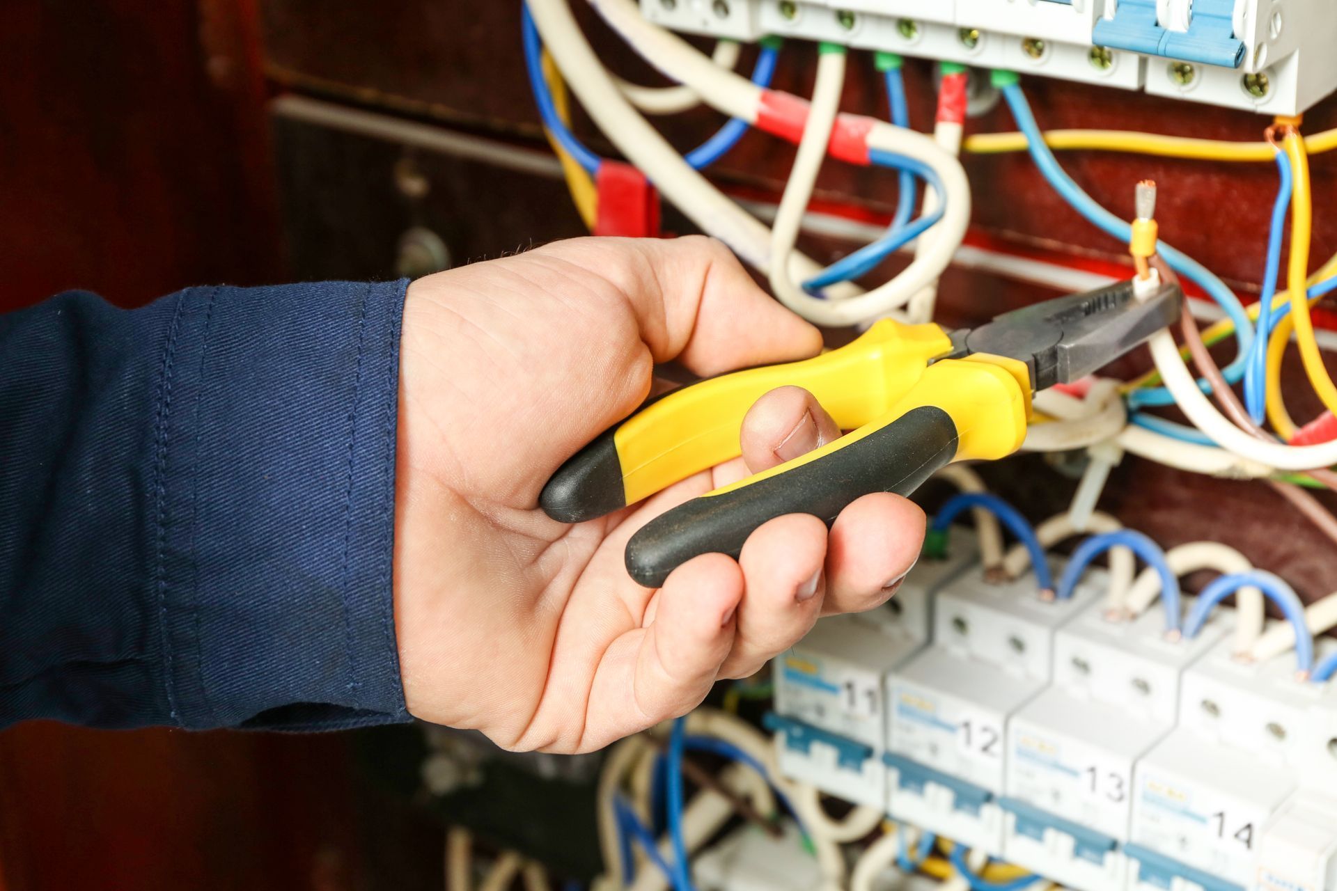 A person is working on an electrical box with a pair of pliers.