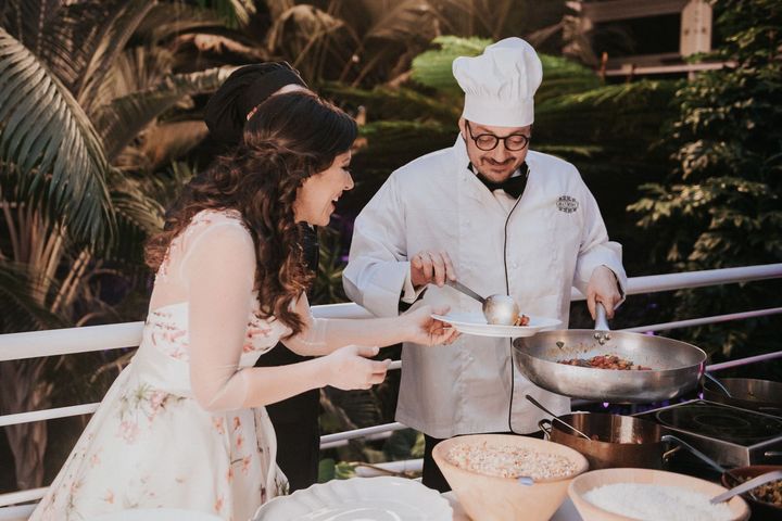 Un uomo con un cappello da cuoco sta cucinando per una donna in abito da sposa.