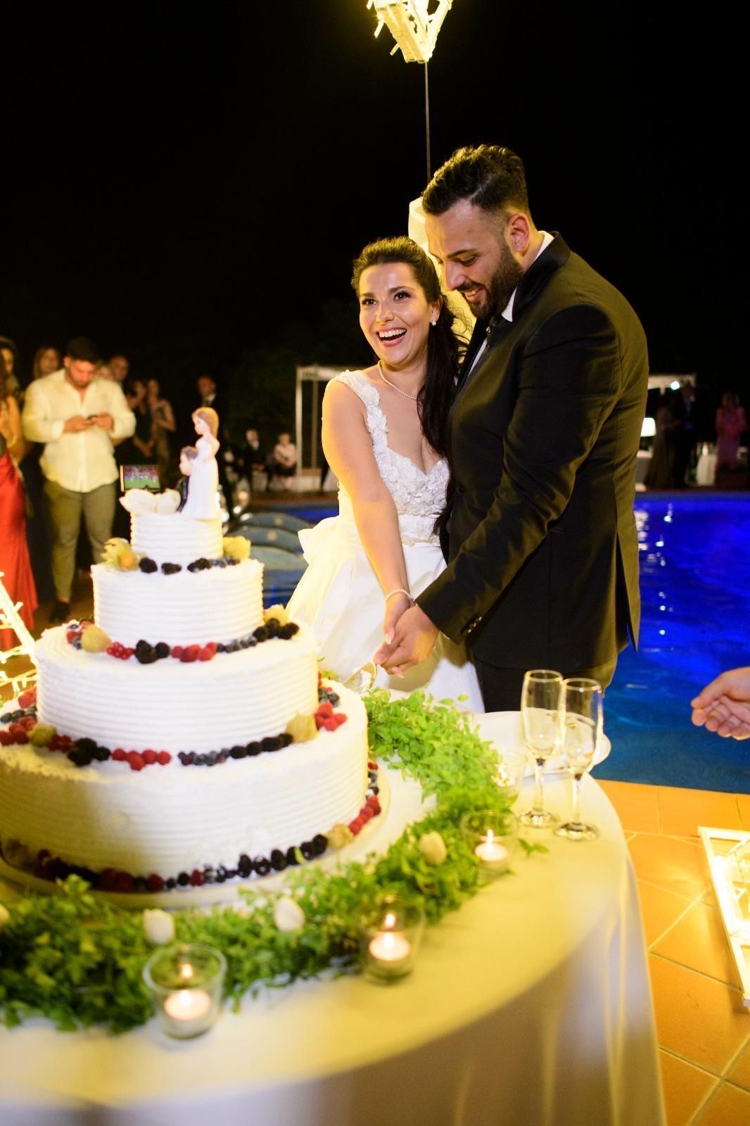 Una coppia di sposi taglia la torta nuziale davanti a una piscina.