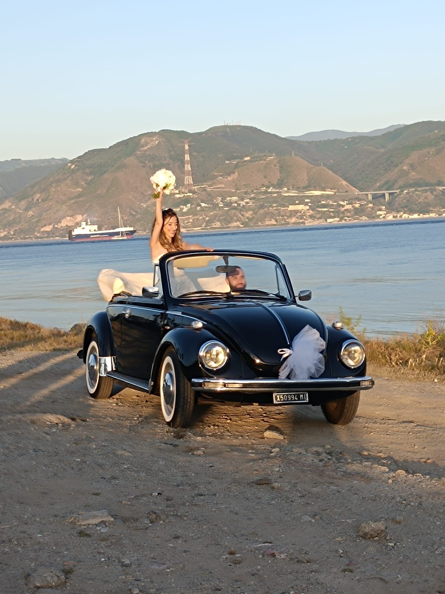 Una sposa e uno sposo sono seduti in un'auto decappottabile nera.