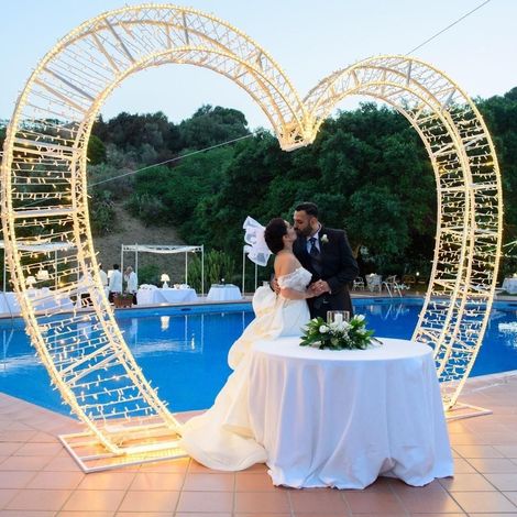 Una sposa e uno sposo che si baciano davanti a un arco a forma di cuore