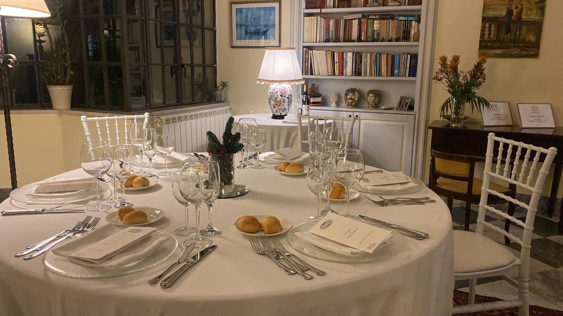 Una tavola rotonda è apparecchiata con piatti, utensili e bicchieri da vino.