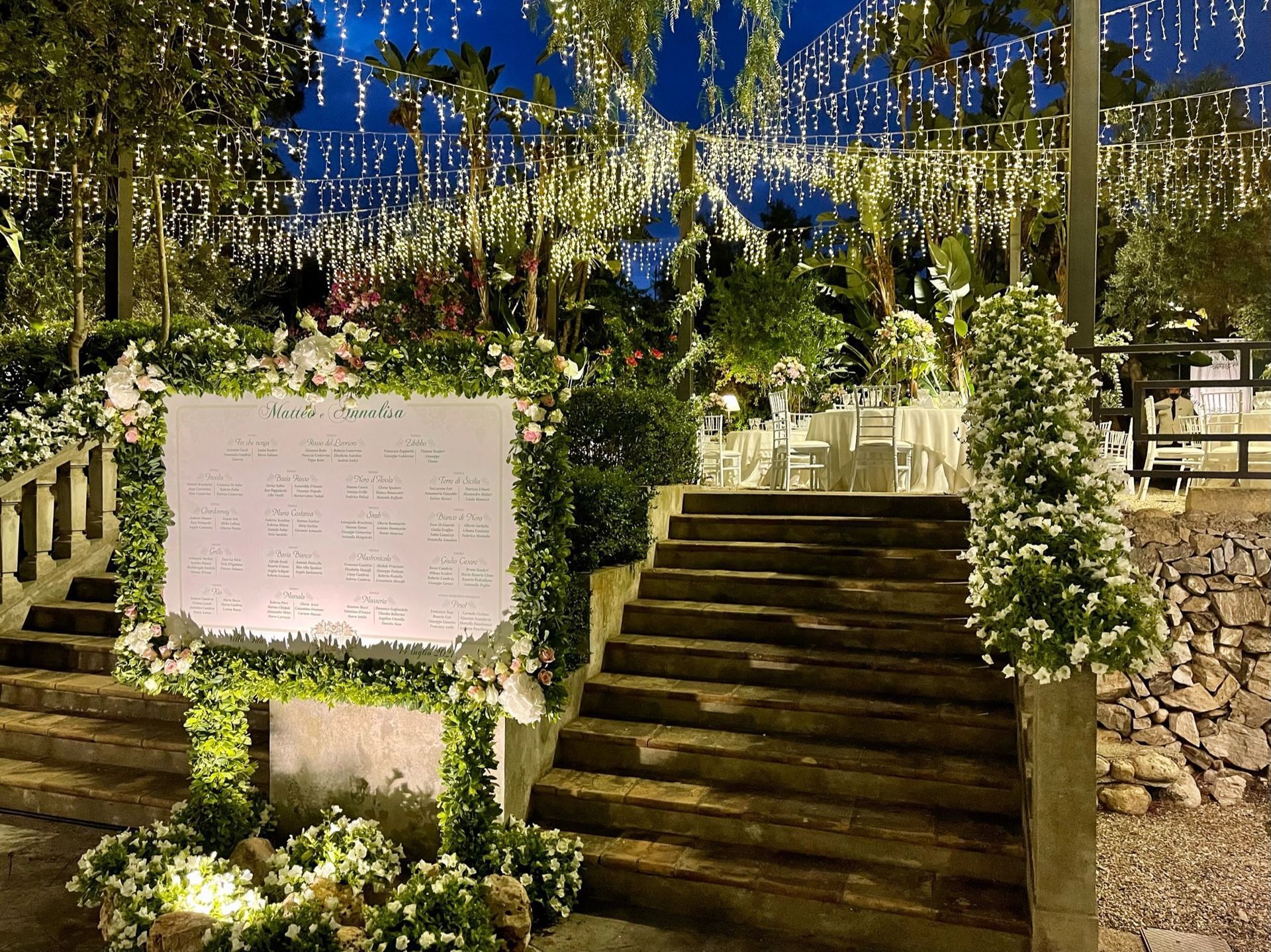 Un cartello sul lato di una scalinata circondata da fiori e luci.