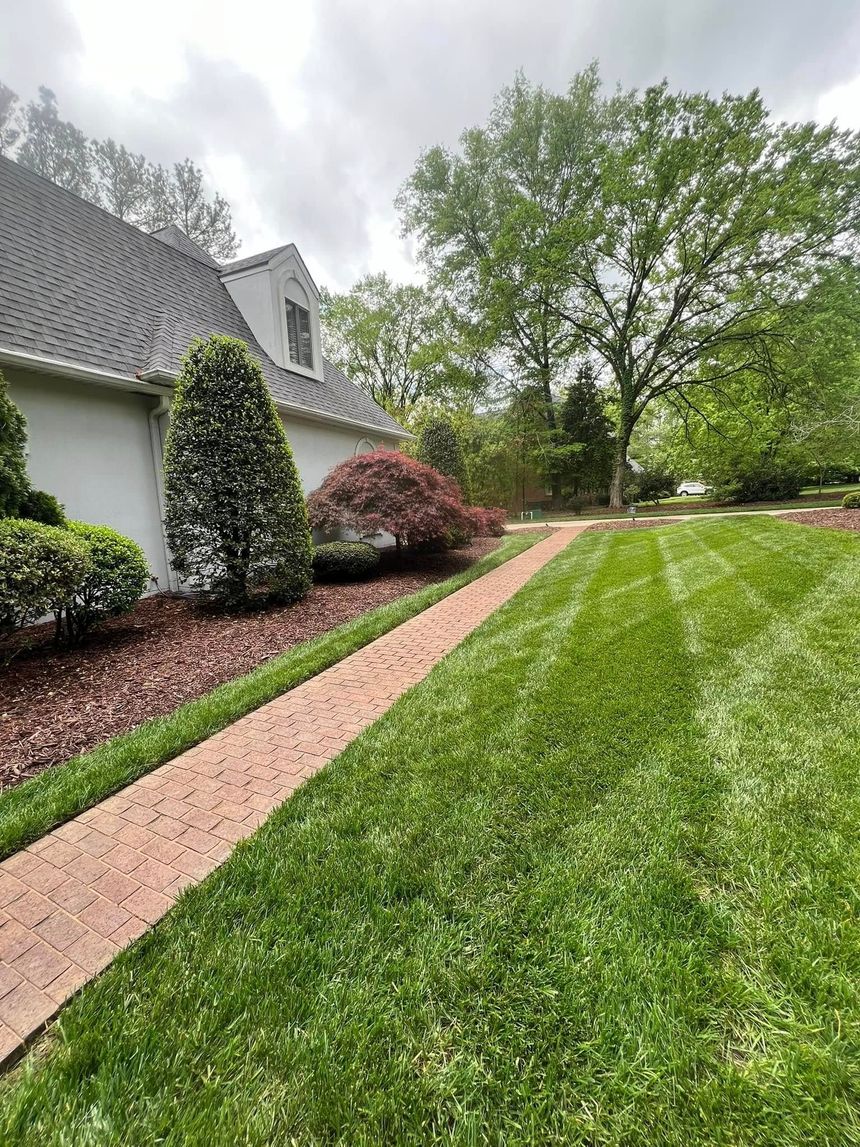 Brick path alongside a house with green lawn and landscaping. Cloudy sky overhead.