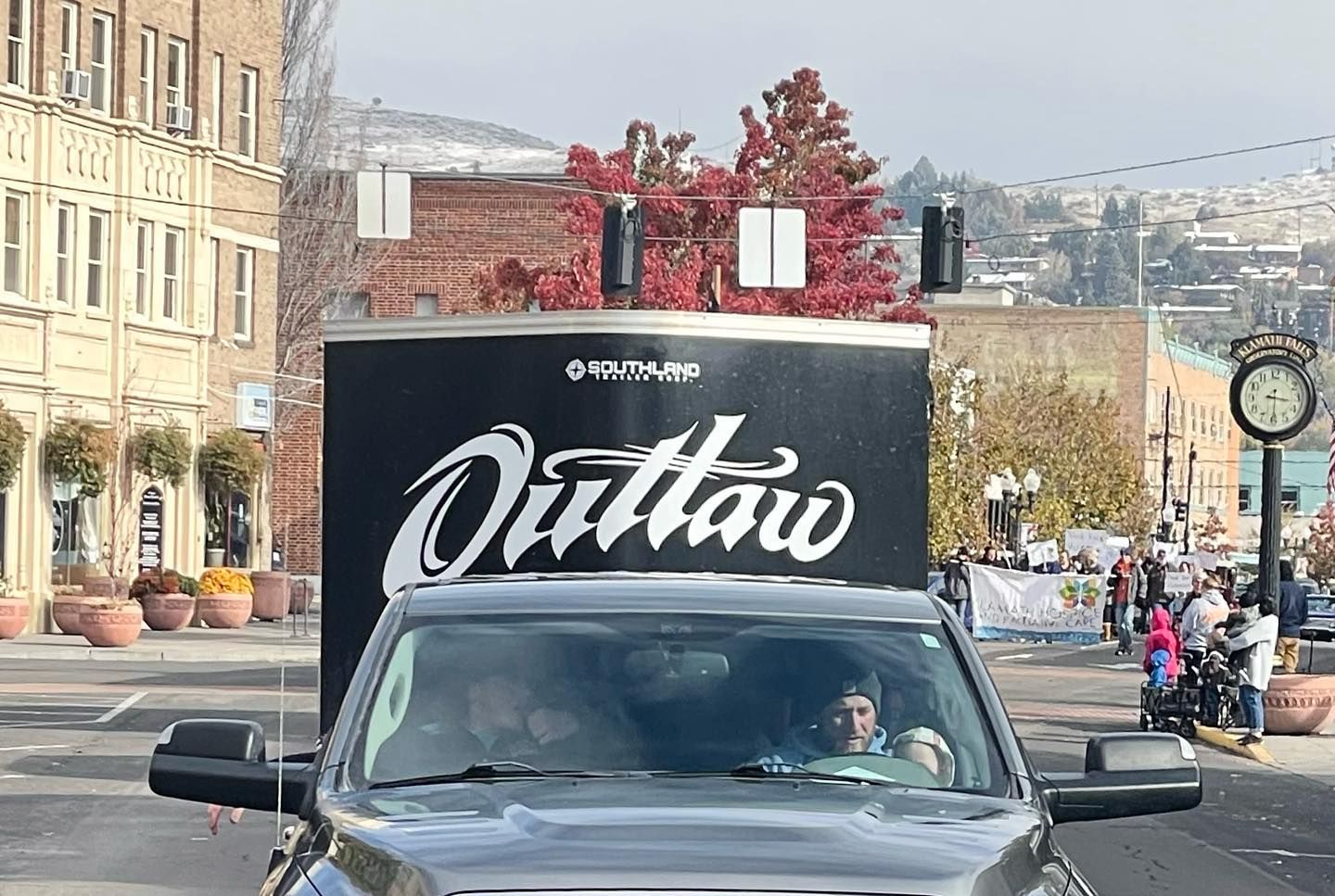 A black truck with the word outlaw on the side is driving down a city street.