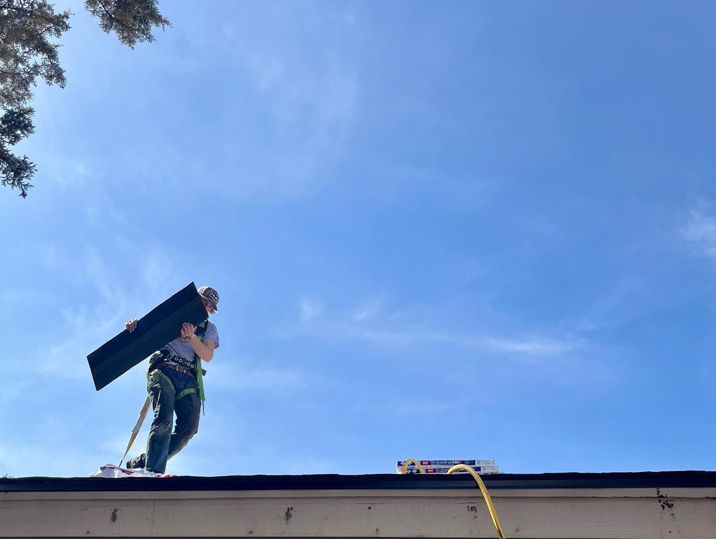 A man is standing on top of a roof holding a piece of wood.