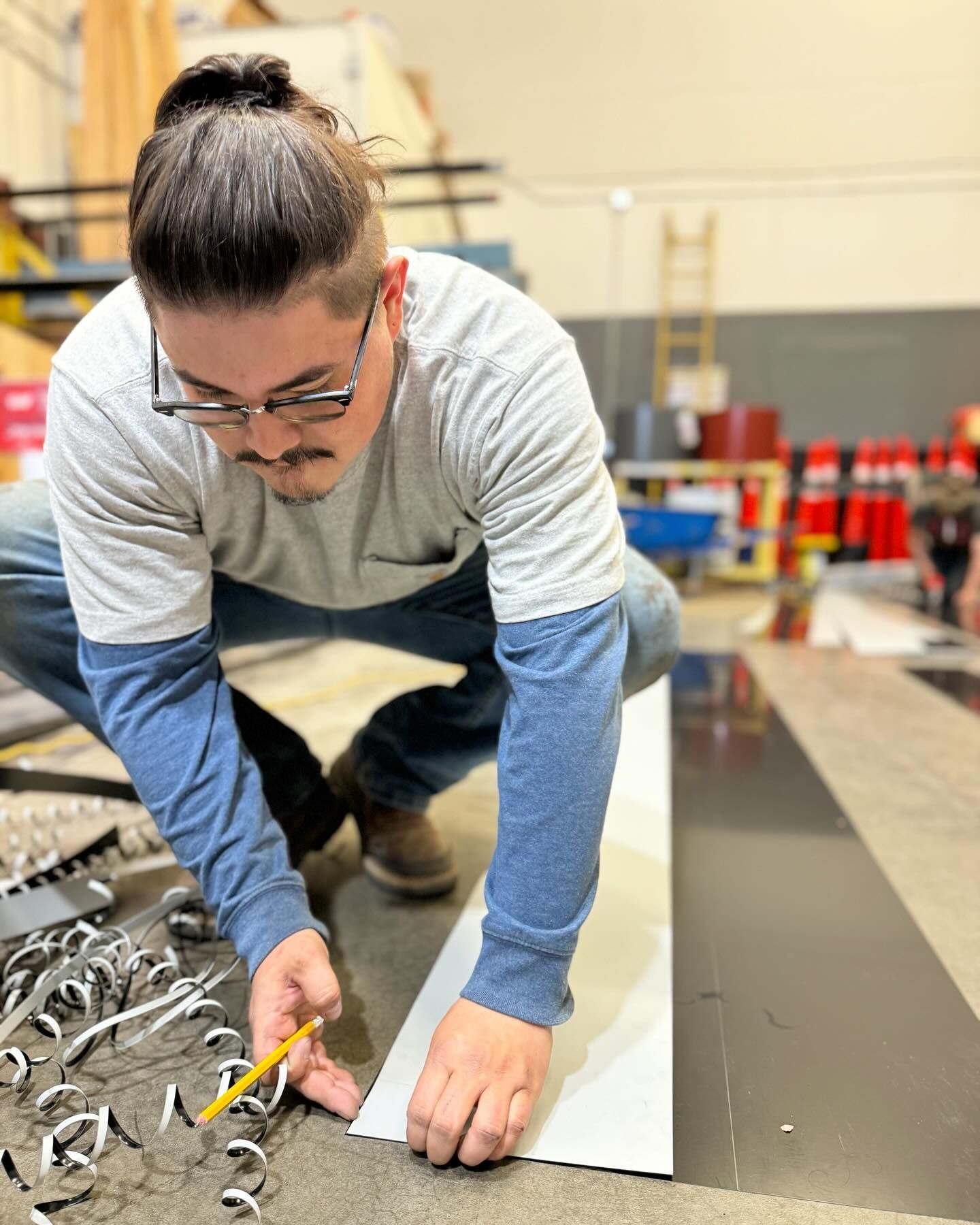A man is measuring a piece of metal with a pencil.