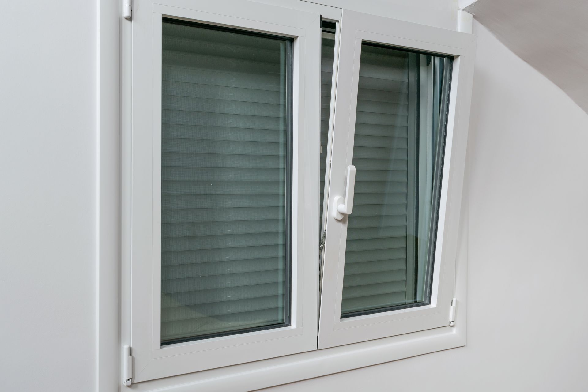 A white window with shutters on it is on a white wall.