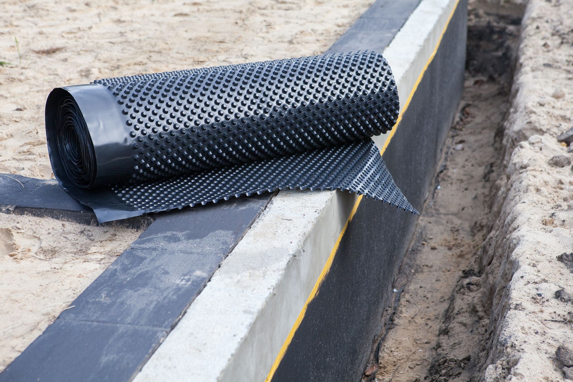 A roll of drainage membrane is sitting on top of a concrete wall.