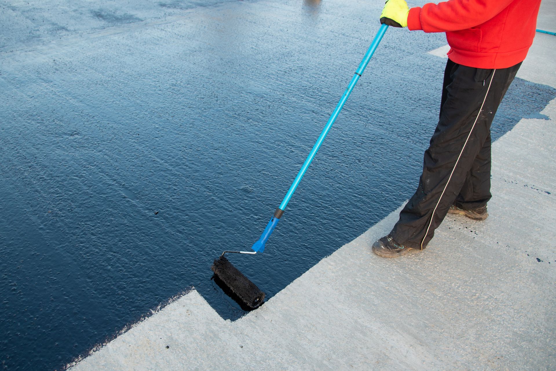 A person is painting a concrete surface with a roller.