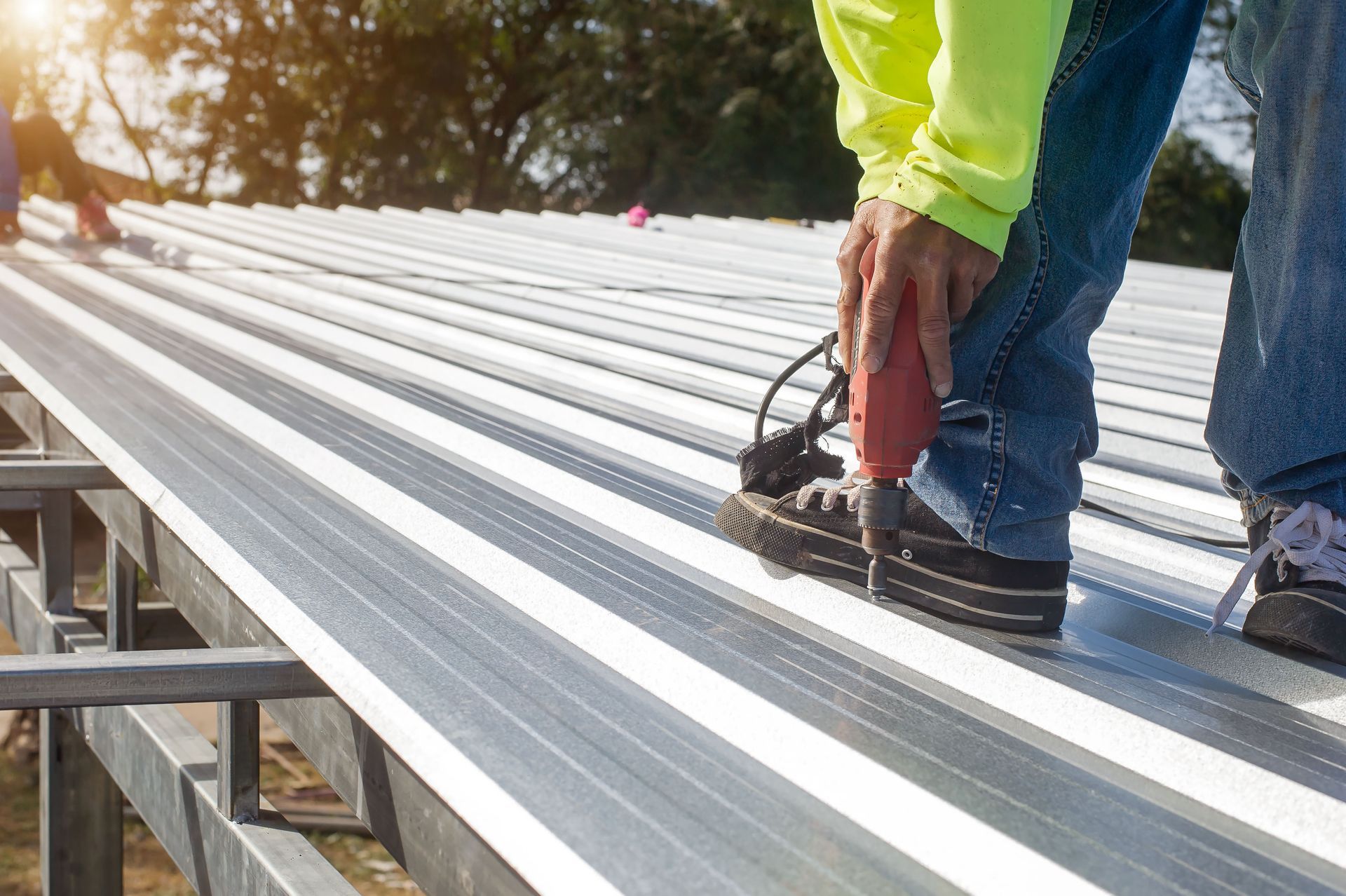 A man is working on a metal roof with a drill.
