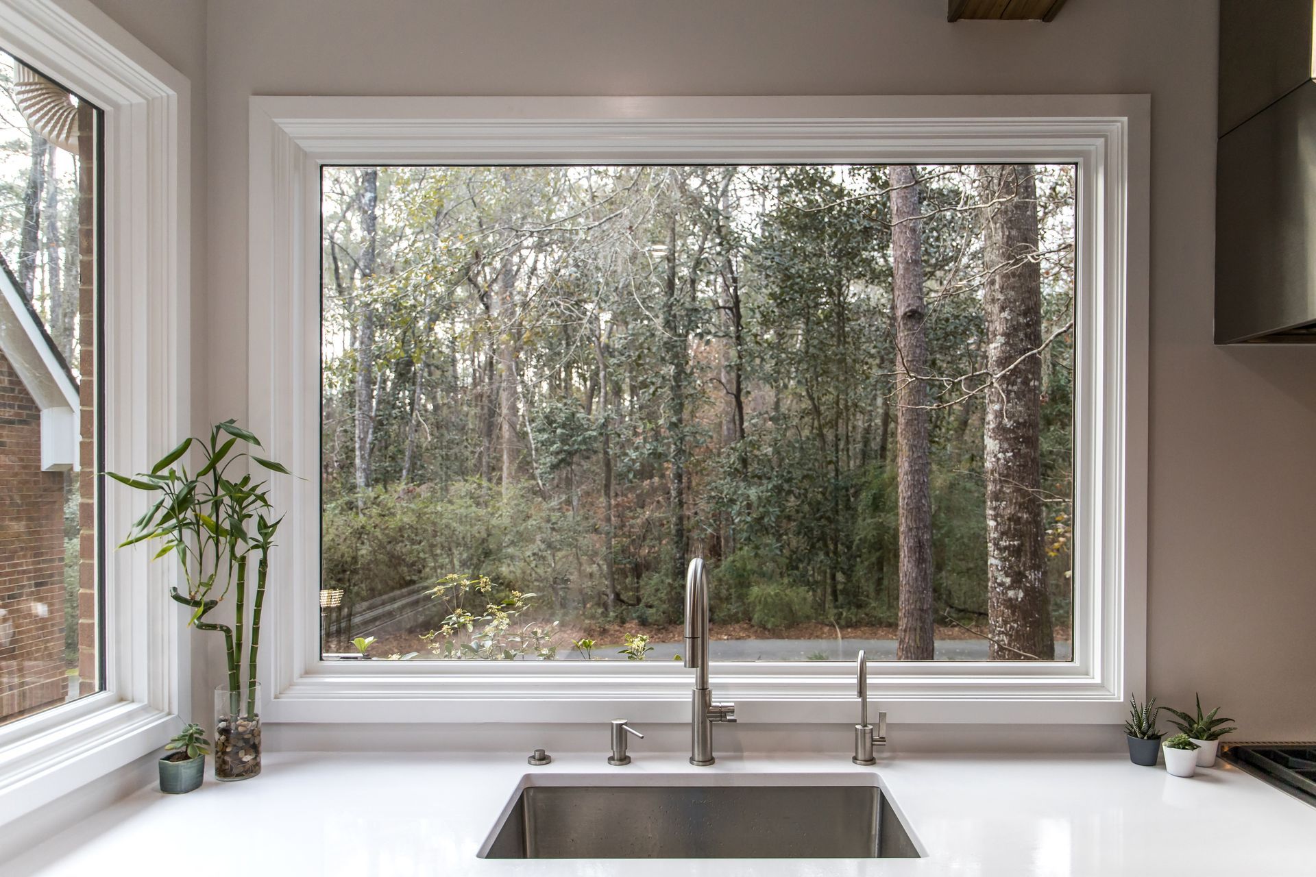 A kitchen sink with a large window overlooking the woods.