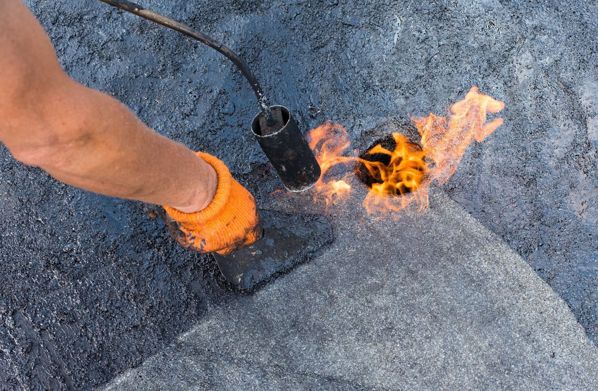 A person is using a torch to heat a piece of asphalt.