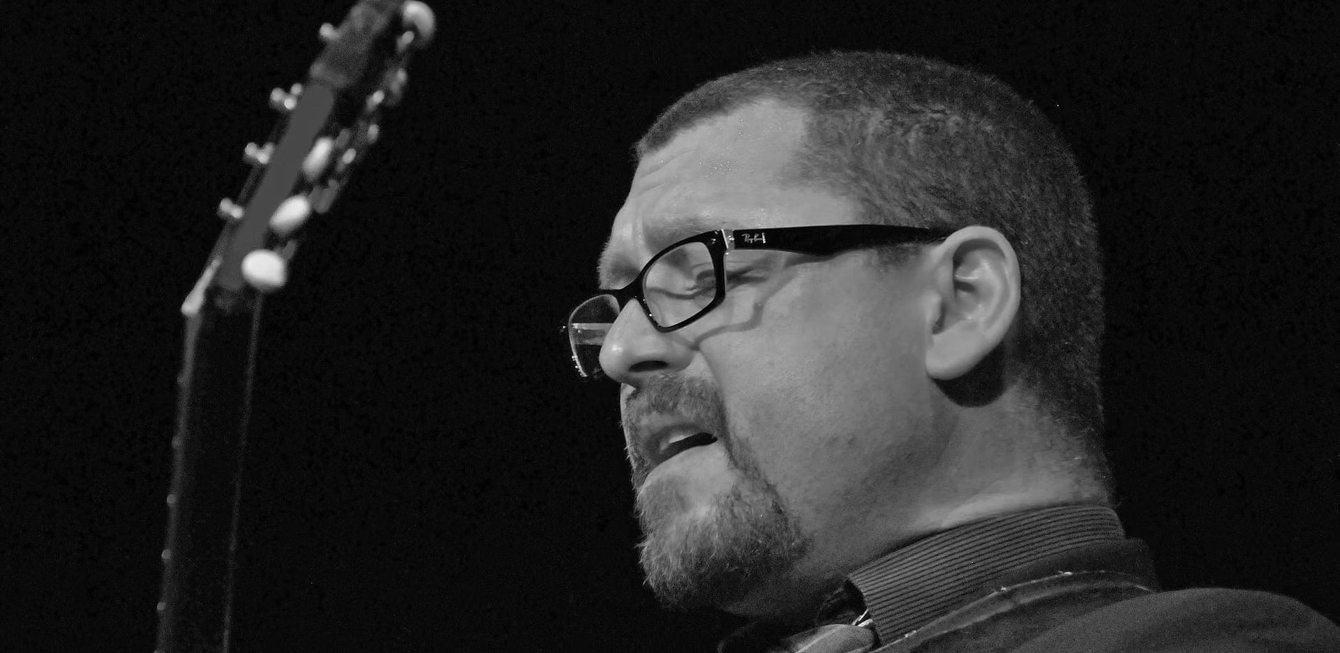 Man in glasses with a guitar, singing. Black and white photo.