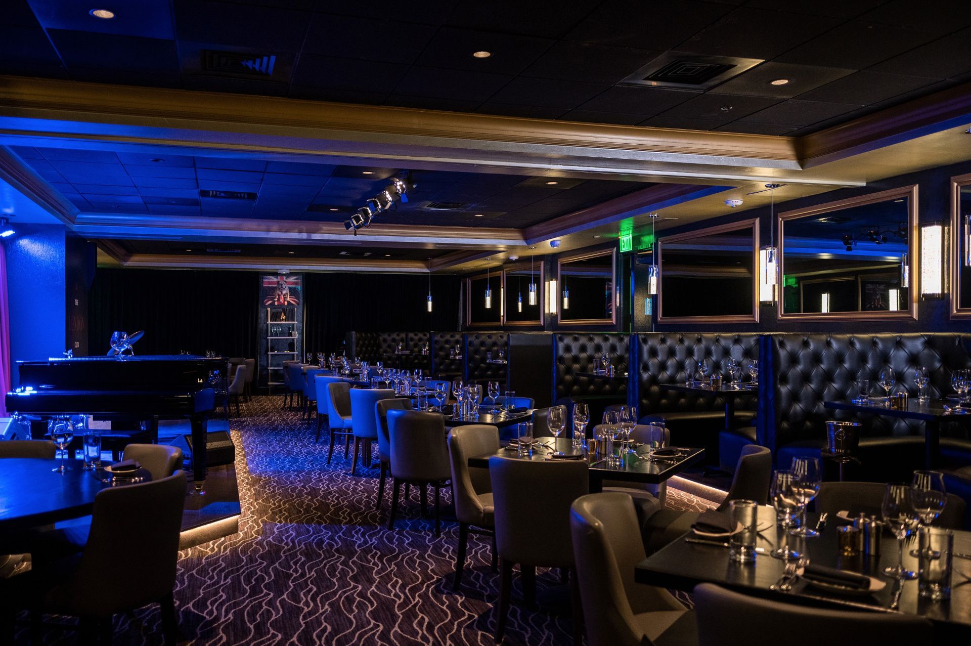 Dimly lit restaurant with tables set for dining, tufted booths, and a piano.