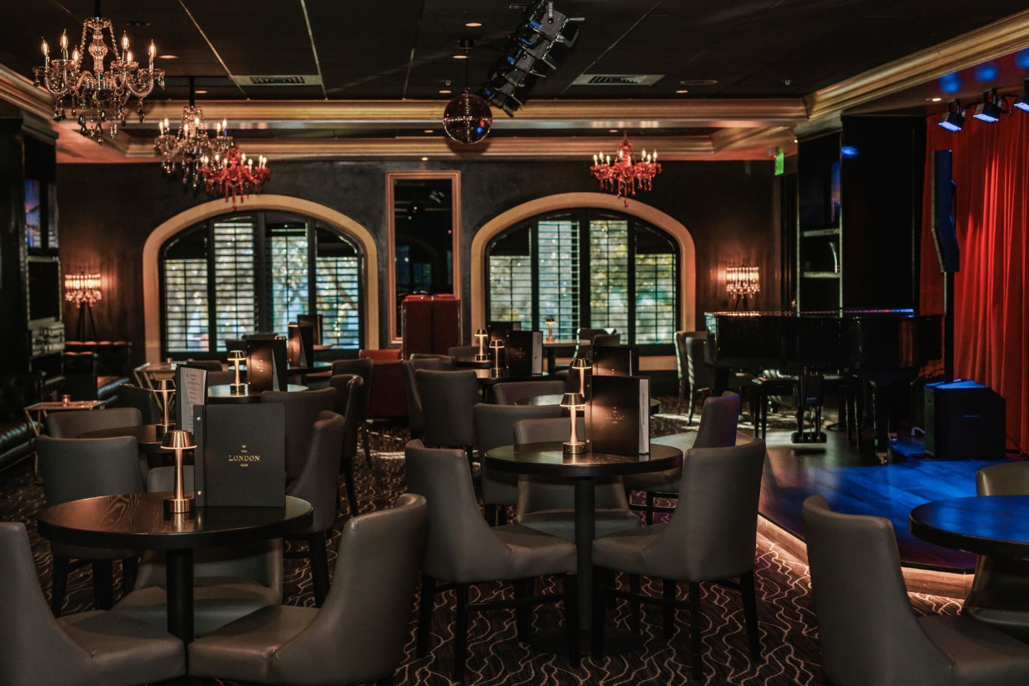 Elegant jazz club interior with tables, chairs, grand piano, stage with red curtain, and decorative lighting.