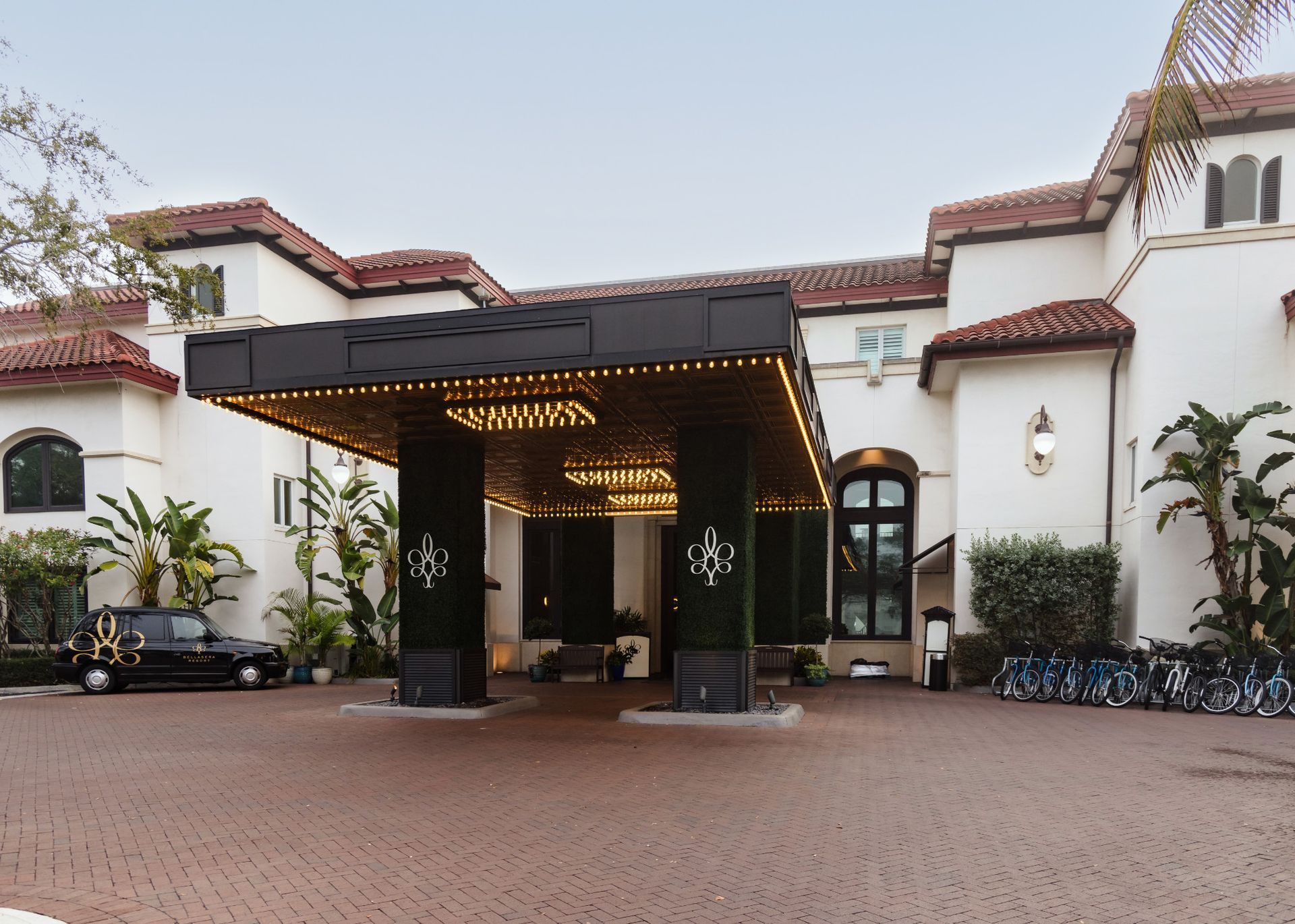 Hotel entrance with covered drop-off area. White stucco building, red tile roof, brick driveway, black car.