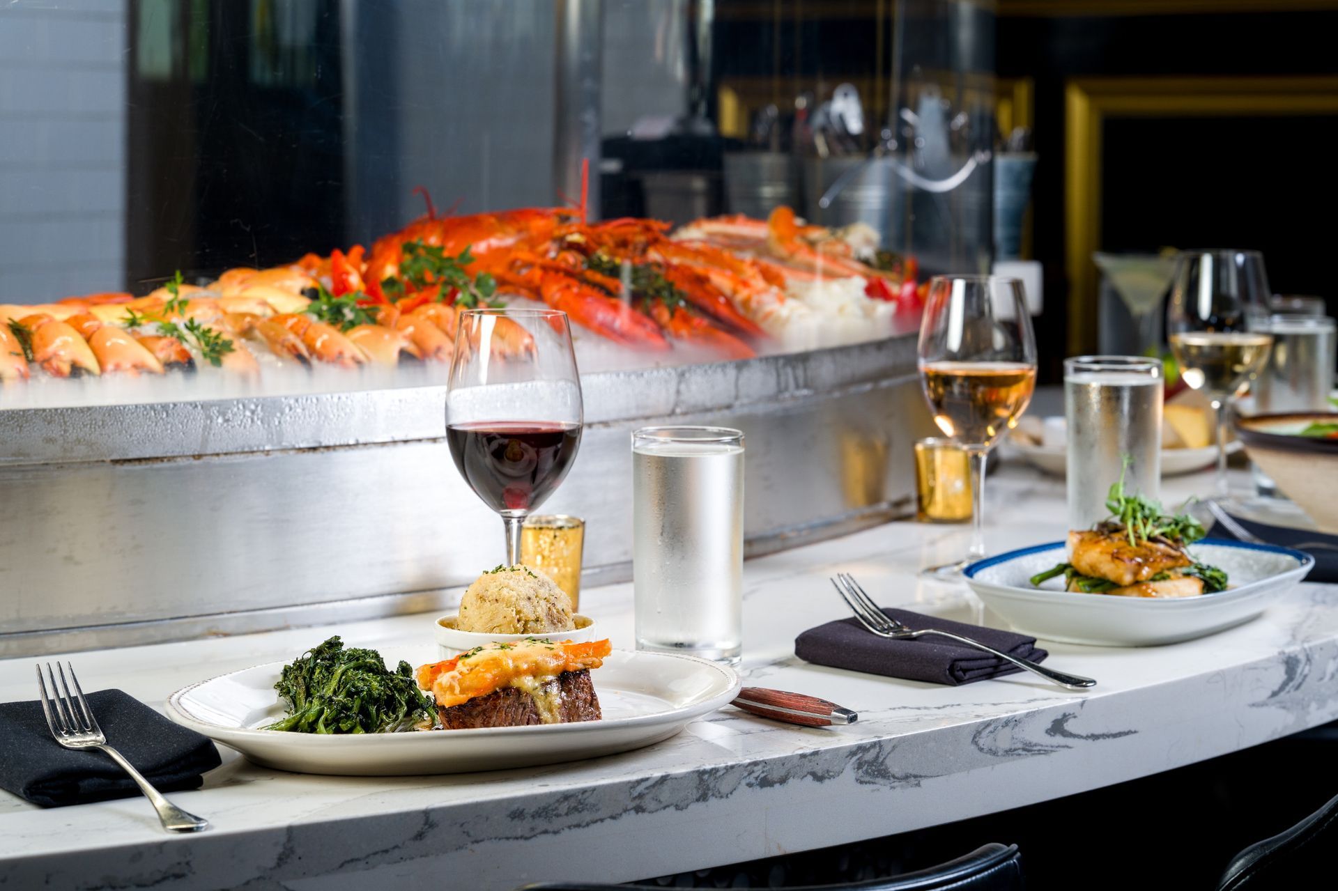 Elegant table setting with lobster on ice, plates of food, and wine glasses.