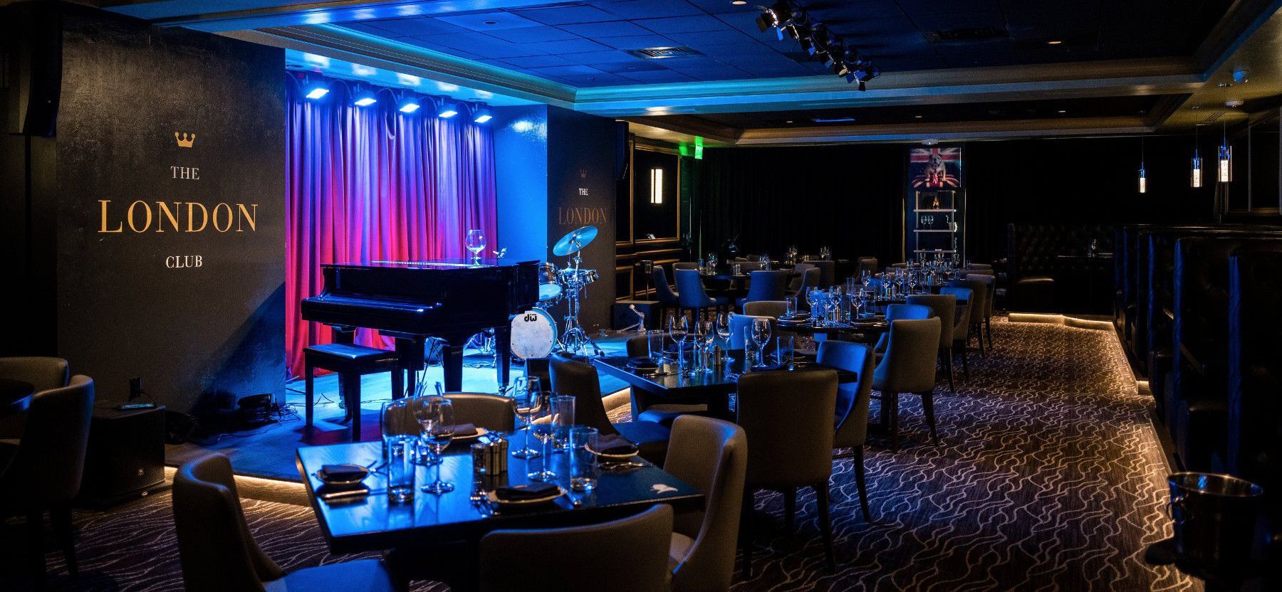 Jazz club interior with piano on stage, tables and chairs. Blue and purple lighting.