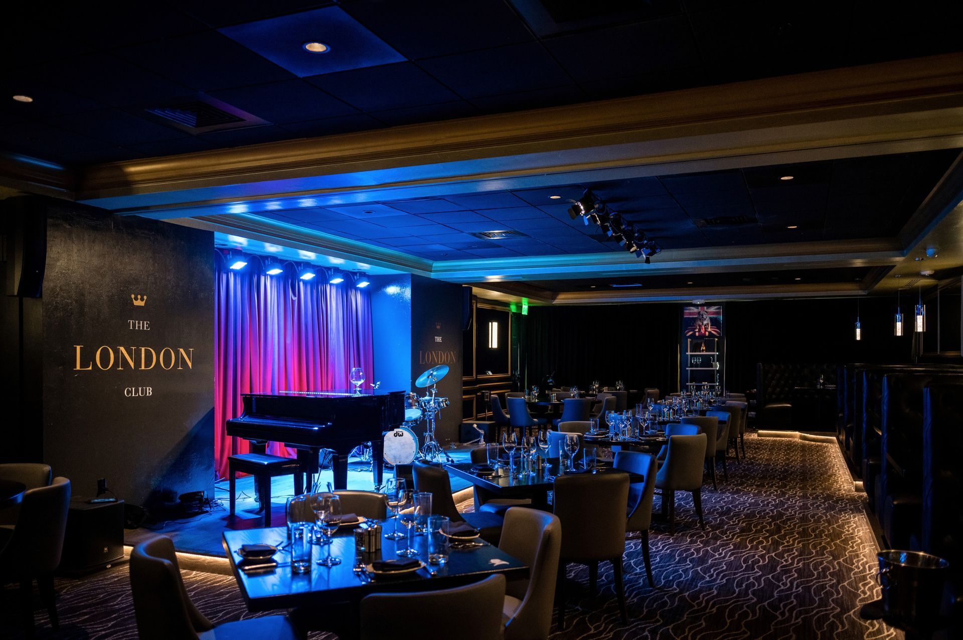 Jazz club interior with piano on stage, tables and chairs. Blue and purple lighting.
