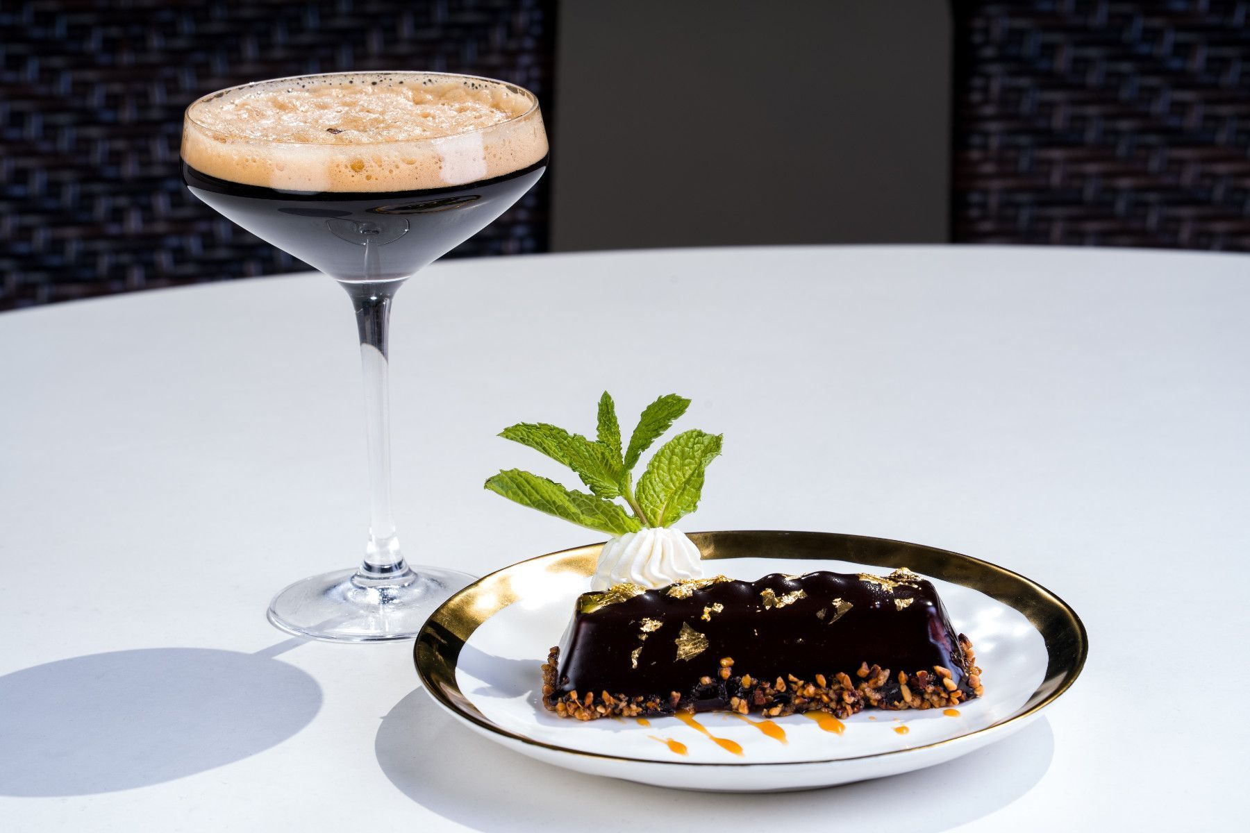 Dark cocktail and chocolate dessert on a white plate with gold trim, garnished with mint.