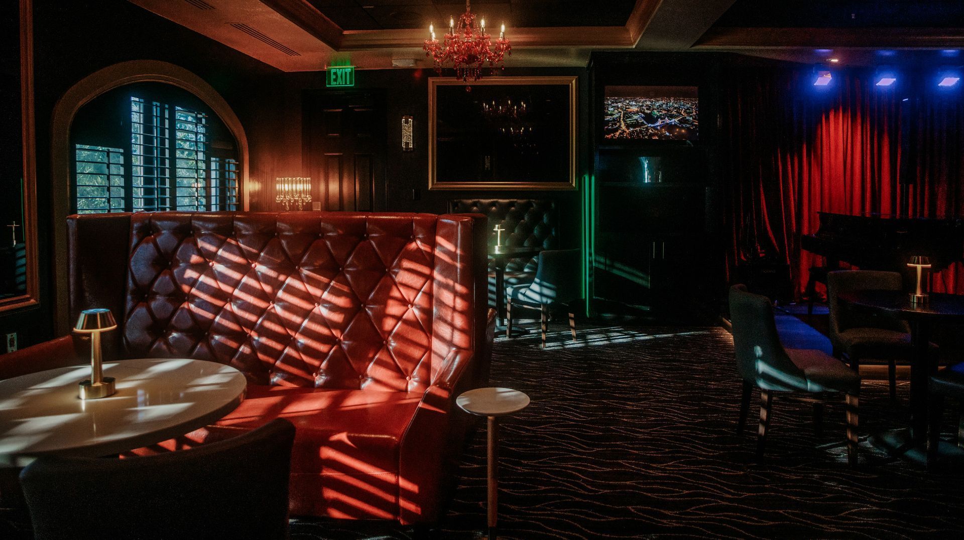 Interior of a dimly lit, luxurious lounge with red booth seating, a small stage, and a chandelier.
