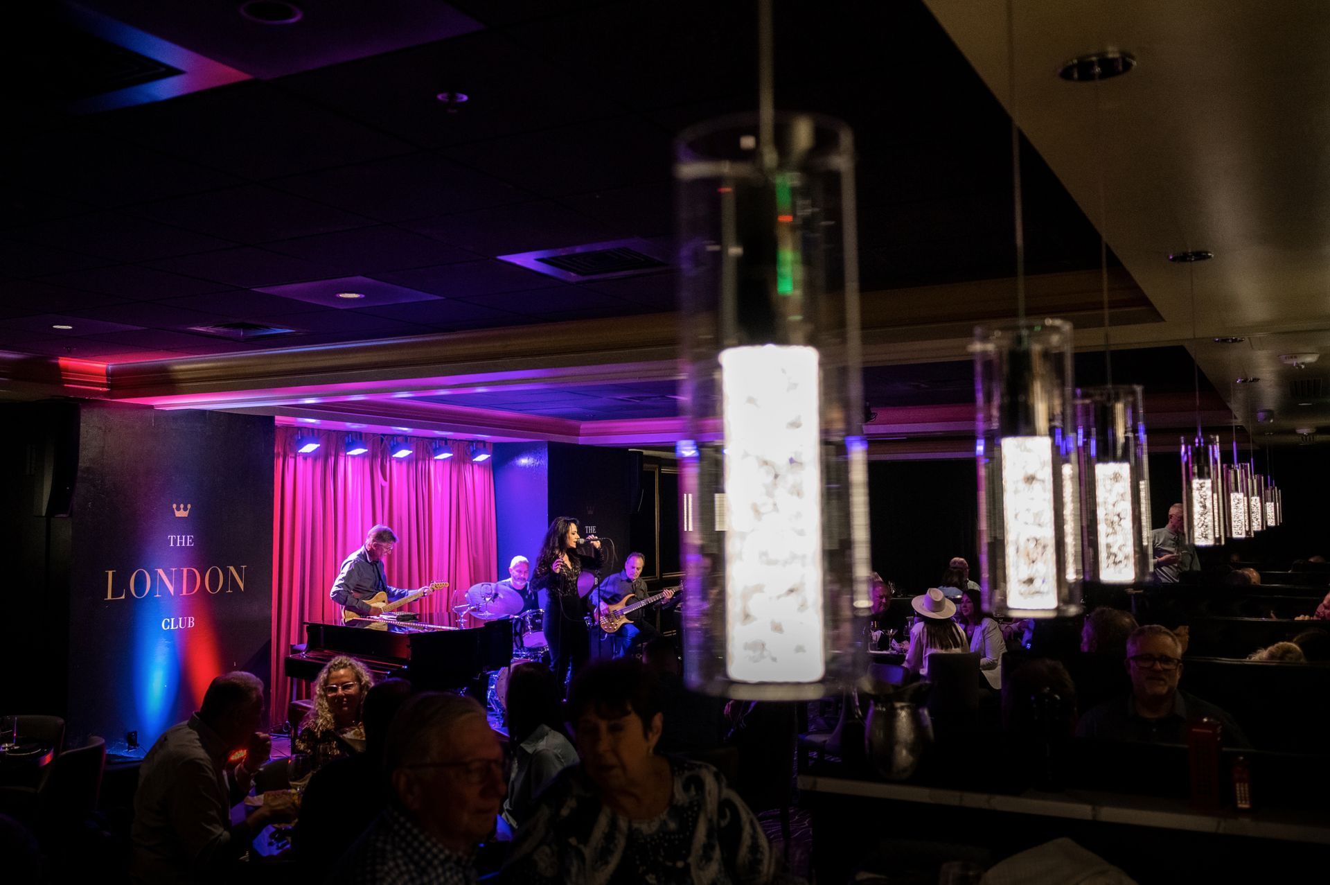 Band performing on stage at a dimly lit London jazz club, with hanging lights and audience.