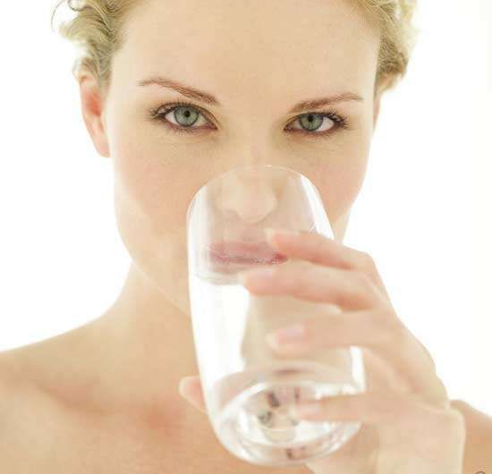 Close-up of a person holding a glass of water and drinking against a white background