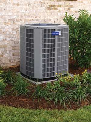 Outdoor air conditioning unit beside a brick wall and shrubs