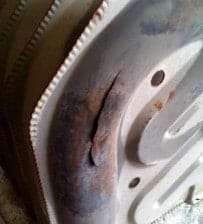 Rusty metal panel with a dark burn or crack mark near a curved edge