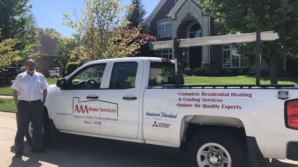 White service pickup truck parked by a house with a man standing beside it in bright daylight