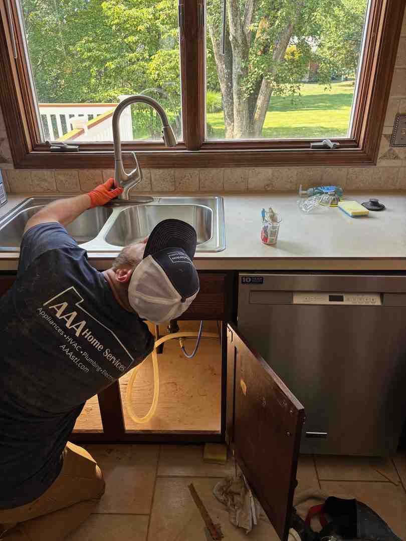 Person installing a kitchen sink faucet under a window in a bright kitchen