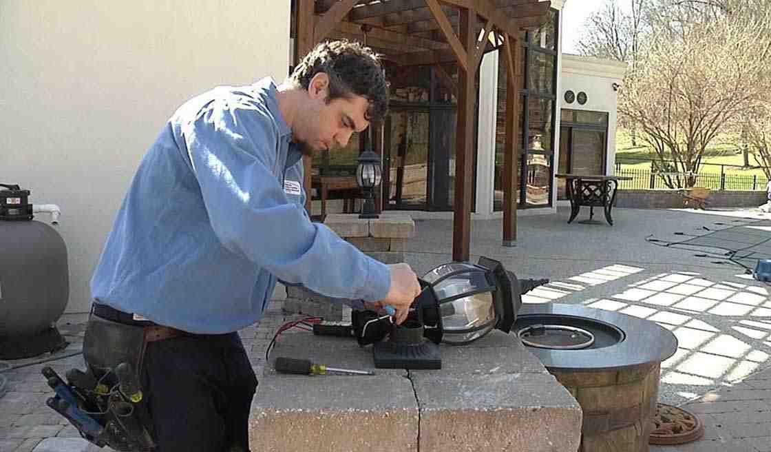 Man in blue shirt using a saw to cut wood on an outdoor workbench under a patio